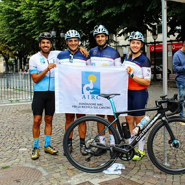 Immagine di tre ciclisti e una ciclista una bici e il logo di AIRC